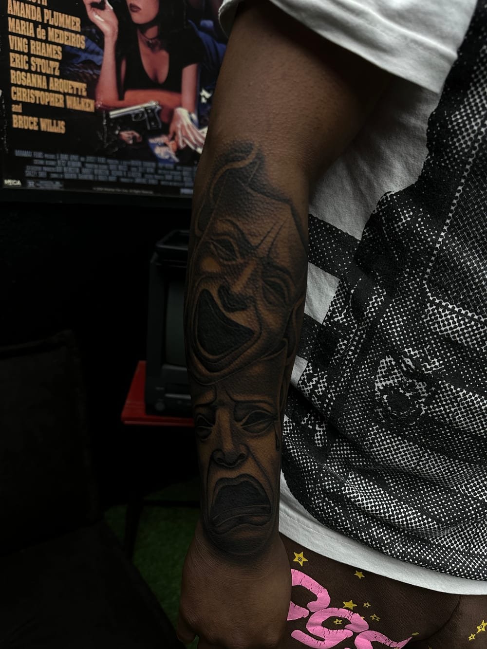 Black and grey theatrical comedy and tragedy masks covering a forearm.