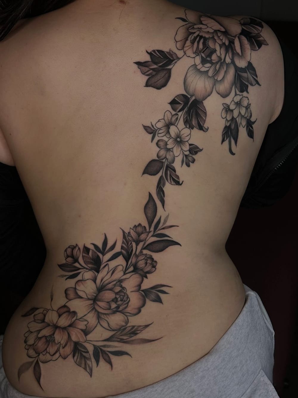Black and grey floral piece running the length of a back and spine.