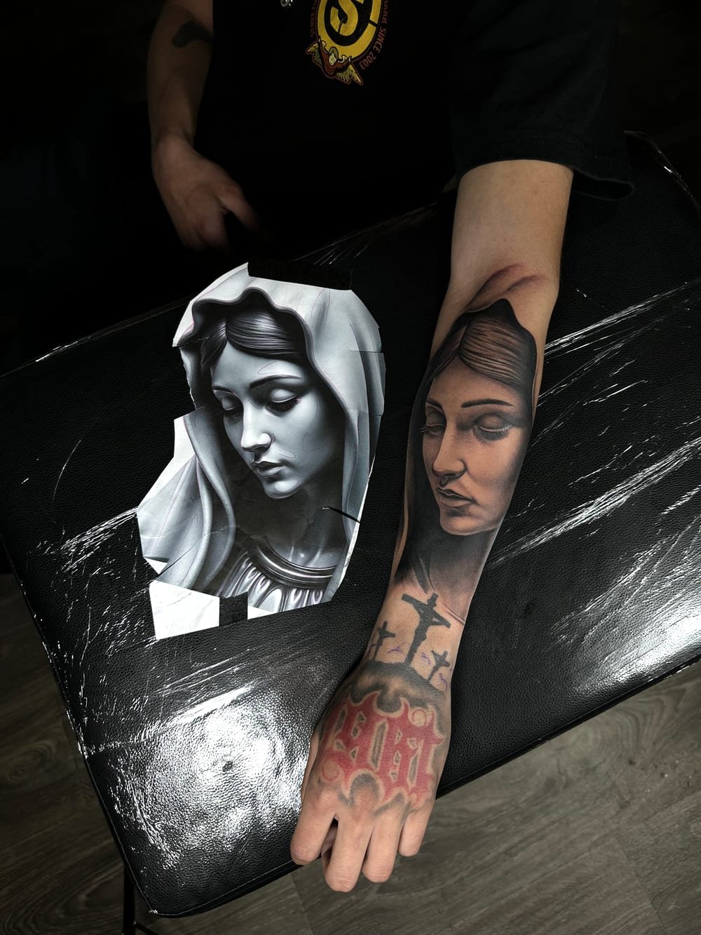 Black and grey Virgin Mary portrait running down a forearm onto the hand.