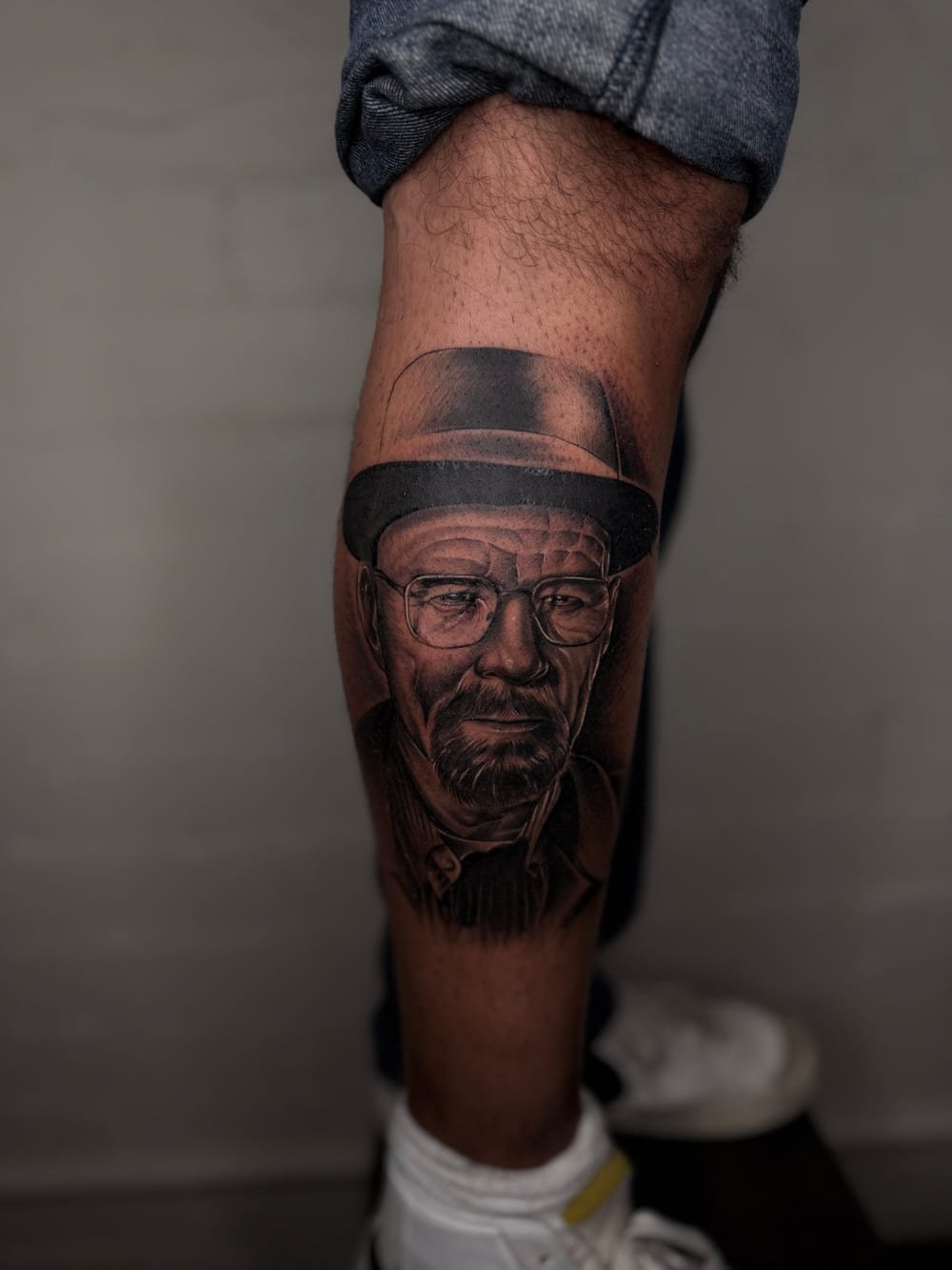 Black and grey portrait of a bearded man in a hat and glasses down a calf.