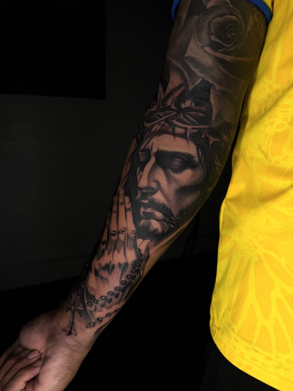 Black and grey portrait of Christ with a rosary along a forearm.